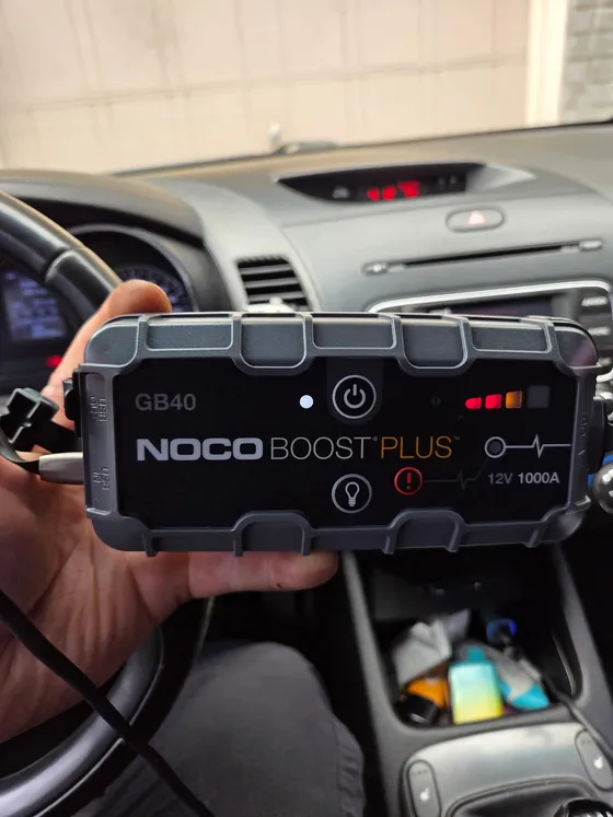 Lithium jump pack held inside a car during a no-start call, dashboard visible through the windscreen