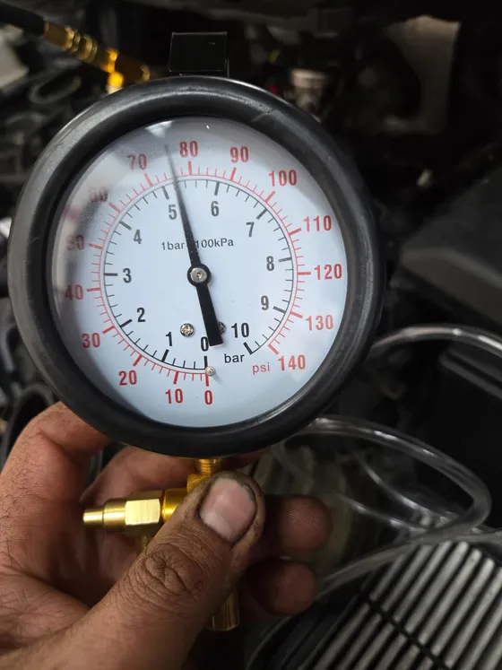 Pressure test gauge held against an engine, reading in both bar and psi during a fault diagnosis
