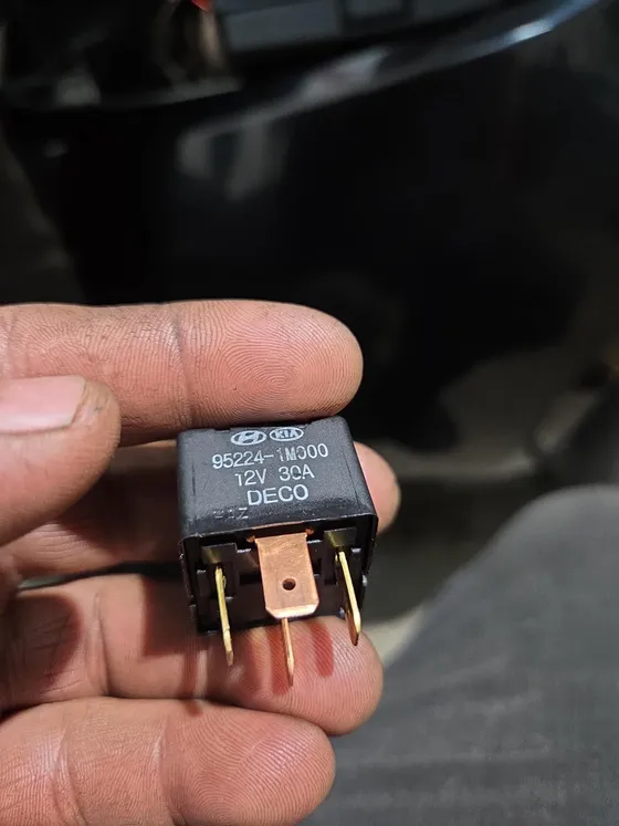 Twelve-volt relay held in hand after being pulled from a vehicle fuse box for testing