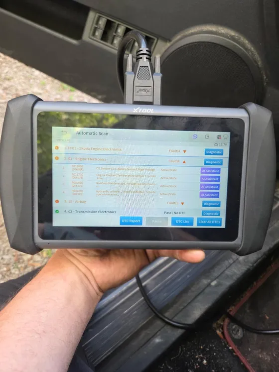 Diagnostic scan tool held up beside a car, showing four active engine fault codes including an oxygen sensor circuit and a coolant temperature sensor