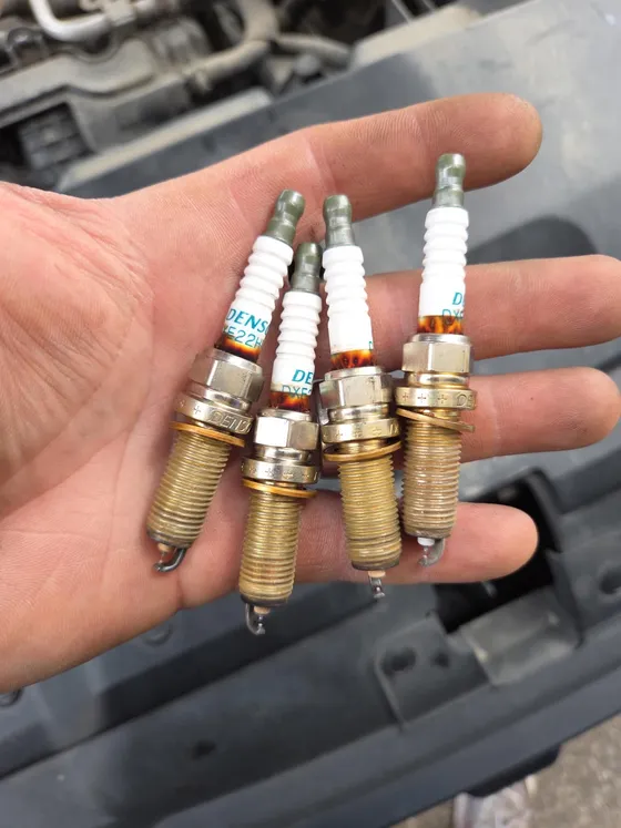 Four used spark plugs held in one hand after removal, ready to be compared against new ones