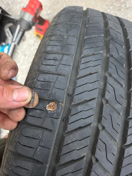 Tyre tread being checked by hand at the roadside with a cordless tool and tyre plug kit alongside